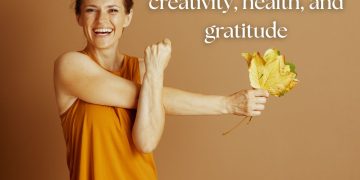 Smiling woman in warm autumn tones holding golden leaves, symbolizing autumn activities and seasonal wellbeing.