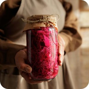 Hands holding a jar of homemade fermented cabbage as part of traditional autumn activities.